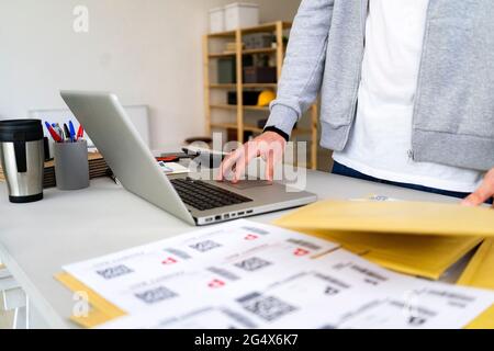 Männlicher Profi mit Paketsuche auf Laptop im Büro Stockfoto