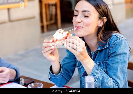 Lächelnde Frau, die im Straßencafé Pizza isst Stockfoto