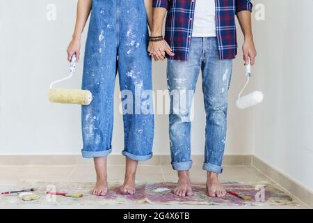Paares with paint Roller Holding hands while standing in New Home Stockfoto