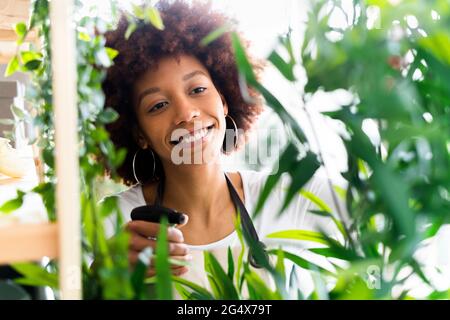 Lächelnde weibliche Floristin, die Wasser auf die Pflanze im Geschäft sprüht Stockfoto