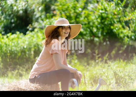 Frau mit Sonnenhut sitzt an sonnigen Tagen im Garten auf Heu Stockfoto