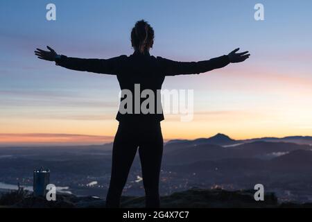 Frau mit ausgestreckten Armen, die während des Sonnenaufgangs im Freien steht Stockfoto