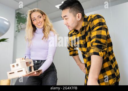 Junger Geschäftsmann im Gespräch mit einer Kollegin, die ein Musterhaus im Amt hält Stockfoto