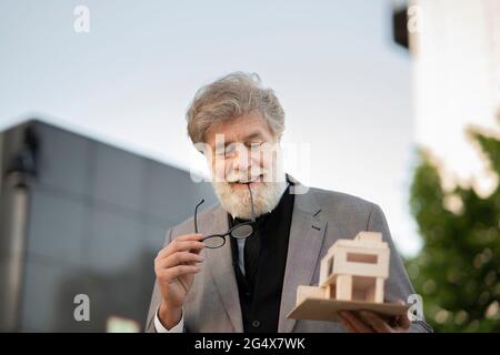 Lächelnder reifer bärtiger Architekt, der das Modellhaus anschaut Stockfoto