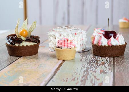 Mini-Sablée-Pasteten mit Schlagsahne und Minitörtchen mit Kirschen und Physalis. Im Hintergrund Mini-Vanillekuchen. Stockfoto