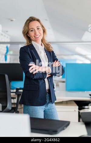 Weibliche Profikerin mit gekreuzten Armen, die im Büro stehen Stockfoto
