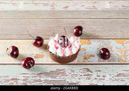 Schokoladen-Mini-Pie mit Schokoladenganache, gekrönt mit Schlagsahne und Kirsche. Umgeben von Kirschen. Stockfoto