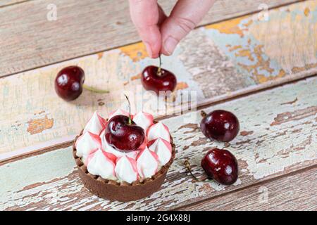 Schokoladen-Mini-Pie mit Schokoladenganache, gekrönt mit Schlagsahne und Kirsche. Im Hintergrund, Süßwaren Platzierung Kirschen. Stockfoto