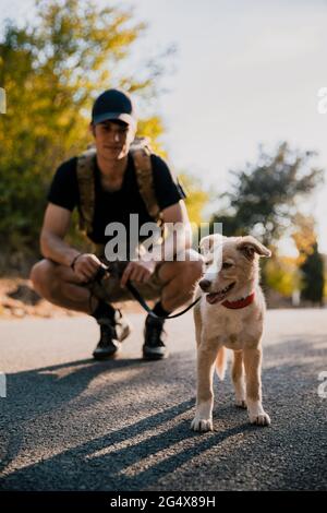 Männlicher Wanderer, der den Hund anschaut, während er auf dem Fußweg hockend Stockfoto