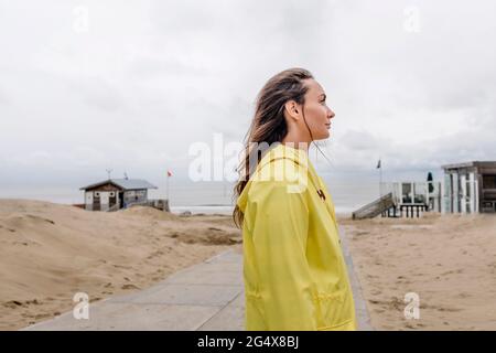 Frau im gelben Regenmantel, die am Strand steht Stockfoto