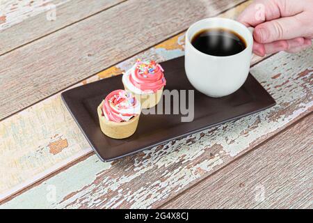 Mini-Pasteten mit Sablée-Gebäck und Schlagsahne, neben einer Hand, die nach einer Tasse Kaffee greift. Stockfoto