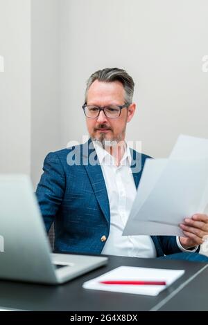 Geschäftsmann mit Dokumenten, die im Büro mit einem Laptop arbeiten Stockfoto