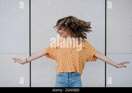 Junge Frau mit ausgestreckten Armen, die Haare vor die Wand werfen Stockfoto