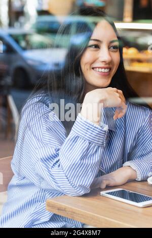 Schöne junge Frau, die in der Bar sitzt und durch das Glas gesehen wird Stockfoto