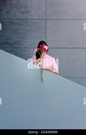 Junge Frau, die sich vor dem Geländer mit Gerbera-Gänseblümchen versteckt Stockfoto