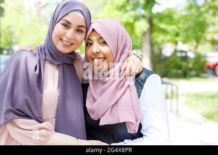 Lächelnde, schöne Frauen mit Händen auf Schultern, die im Park stehen Stockfoto