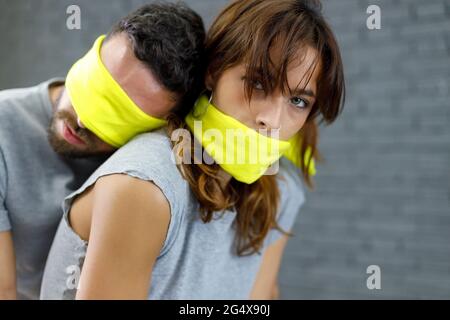 Freund mit verbundenen Augen lehnte sich auf Freundin Mund mit Stoff bedeckt Stockfoto