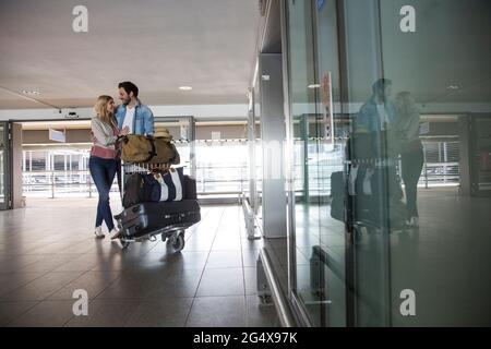 Glückliches junges Paar mit Gepäckwagen am Flughafenterminal Stockfoto