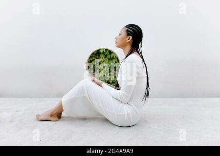 Frau mit geflochtenen Haaren hält den Spiegel, während sie auf dem Boden sitzt Stockfoto