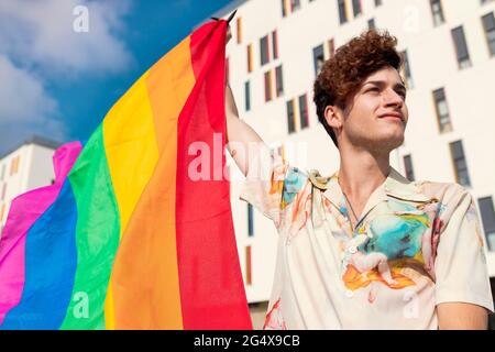 Junger Mann schaut weg, während er Regenbogenfahne bläst Stockfoto