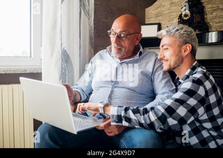 Lächelnder Sohn führt Vater mit Laptop zu Hause Stockfoto
