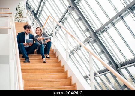Geschäftsmann mit digitalem Tablet, während er auf der Treppe von einem Kollegen sitzt Stockfoto