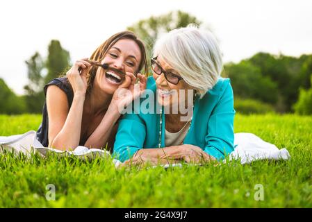 Fröhliche Enkelin, die mit Haaren spielt, während sie bei Großmutter auf der Wiese liegt Stockfoto