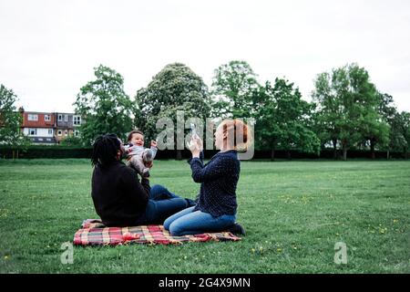 Frau fotografiert verspielten Vater mit Sohn im Park Stockfoto