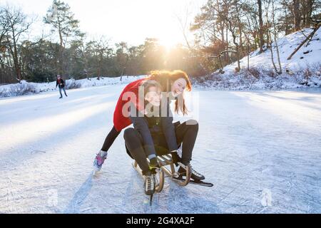 Ein fröhliches Paar genießt Rodeln und Schlittschuhlaufen auf dem gefrorenen See Stockfoto