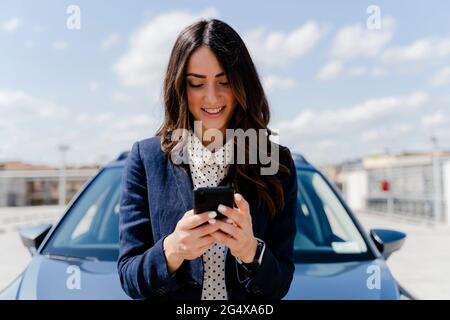 Lächelnde Geschäftsfrau mit Smartphone im Auto Stockfoto