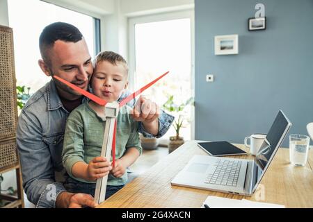 Lächelnder Vater sitzt mit Sohn weht Windturbine zu Hause Stockfoto