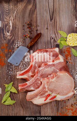 Rohe Schweinekoteletts mit Gewürzen und Hackfleisch auf dunklem Hintergrund. Stockfoto