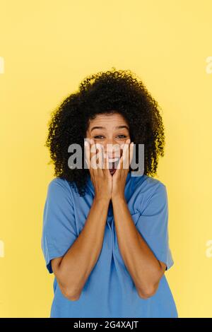 Überraschte Frau, die den Mund mit Händen auf gelbem Hintergrund bedeckt Stockfoto