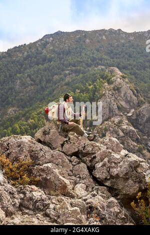 Männlicher Bergsteiger mit Blick auf die Aussicht, während er auf dem Berg sitzt Stockfoto