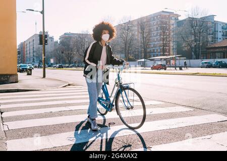 Frau mit Schutzmaske zu Fuß mit dem Fahrrad auf der Straße in der Stadt Stockfoto