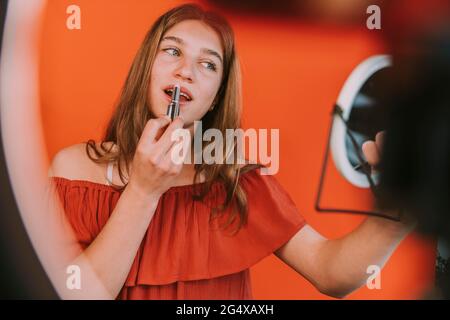 Weibliche Influencerin, die Lippenstift anwendet, während sie zu Hause das Vlogging Make-up Tutorial macht Stockfoto