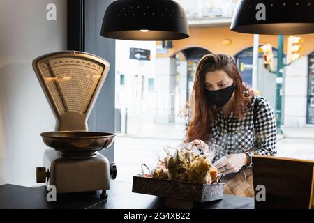 Frau trägt eine schützende Gesichtsmaske und nimmt Lebensmittel vom Tresen im Supermarkt Stockfoto