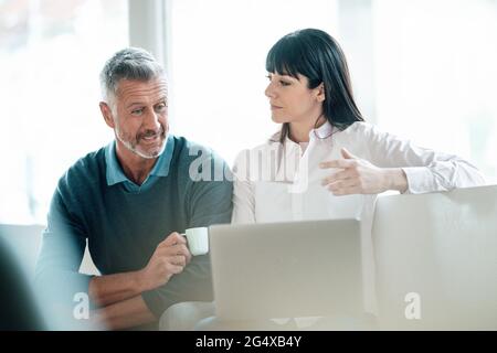 Reife Kollegen, die im Café mit einem Laptop sitzen und diskutieren Stockfoto