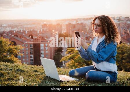 Junge Frau mit Smartphone im Park sitzen Stockfoto