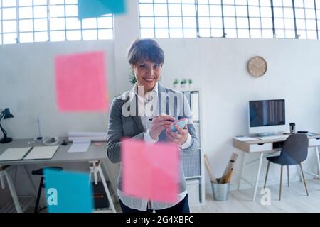 Lächelnde Geschäftsfrau, die im Büro auf Haftnotizen schreibt Stockfoto