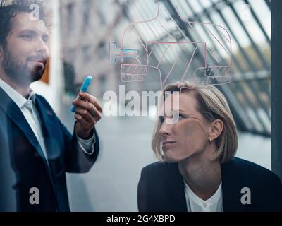 Gelangweilte Geschäftsfrau, die sich an einer Glaswand lehnte, während ein Geschäftsmann im Büro über ein Diagramm sprach Stockfoto