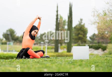 Junge Frau beim Stretching beim Betrachten Tutorial auf Laptop im Park Stockfoto