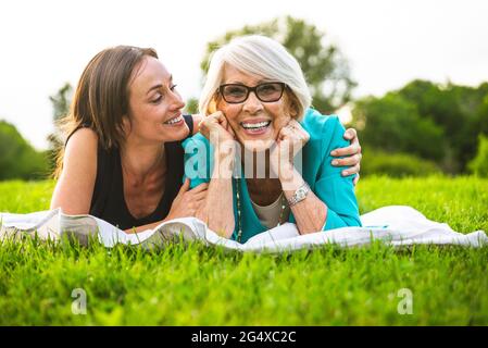 Lächelnde Enkelin mit Arm um die Großmutter, die auf einer Picknickdecke ruht Stockfoto