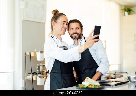 Glückliche Köche nehmen Selfie mit dem Handy in der Küche des modernen Restaurants Stockfoto