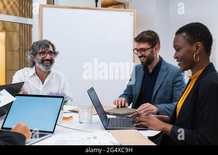 Lächelnde Unternehmer und Unternehmerinnen diskutieren während der Arbeit am Tisch im Büro Stockfoto