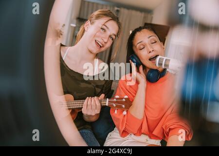 Mädchen spielt Ukulele, während Frau zu Hause am Mikrofon singt