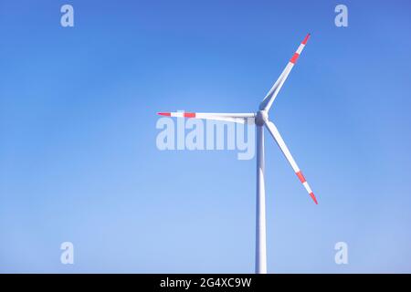 Windturbine, die gegen den klaren blauen Himmel steht Stockfoto