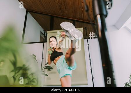 Weibliche Fitnesstrainer, die beim Vlogging zu Hause High Kicks unterrichtet Stockfoto