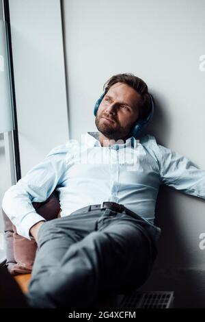 Ein Geschäftsmann mit Kopfhörern schaut weg, während er sich im Büro ausruht Stockfoto