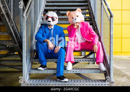 Mann und Frau tragen lebhafte Anzüge und tragen Masken, die auf Metalltreppen sitzen Stockfoto